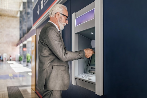 Zdjęcie widok profilu starszego przedsiębiorcy w garniturze za pomocą bankomatu do wypłaty gotówki