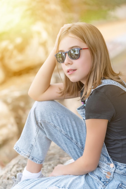 Photo teenage girl with sunglasses and casual clothes sitting looking at the horizon