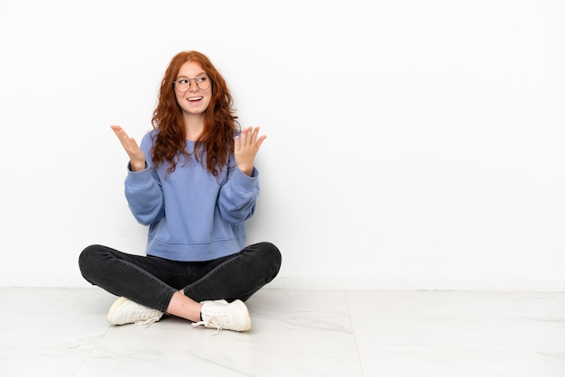 Photo teenager redhead girl sitting on the floor isolated on white background with surprise facial expression