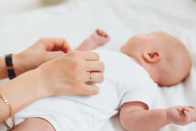 사진 아기는 2개월 동안 침대에 누워 있습니다. 아기의 배에 엄마의 손이 있습니다. 신생아