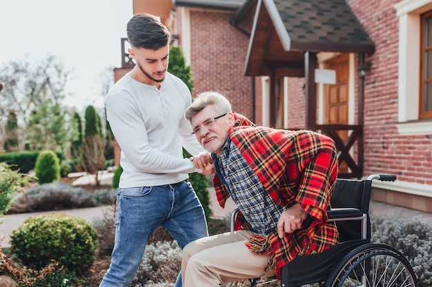 Фото Старик на инвалидной коляске и его сын гуляют по саду, а мужчина помогает своему престарелому отцу.