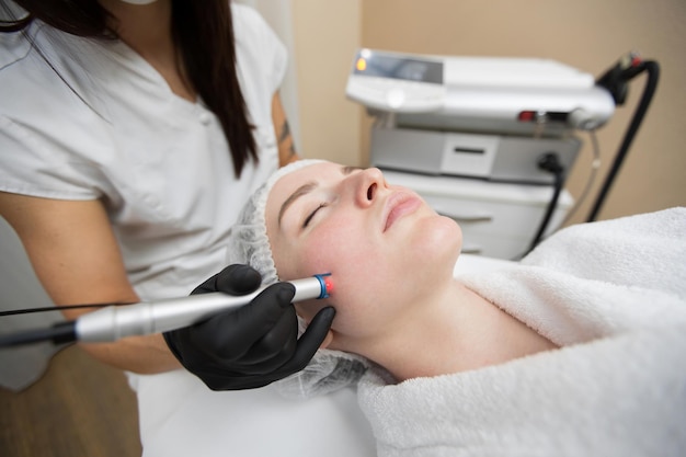 Therapist beautician makes a laser treatment to young womans face at beauty SPA clinic
