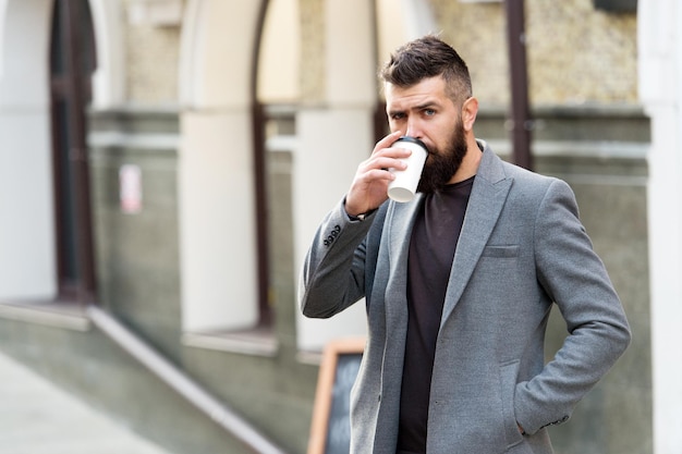Time to drink. Bearded man drinking morning coffee. Hipster with disposable paper cup walking in city. Businessman in hipster style holding takeaway coffee. The best time of day to drink coffee.