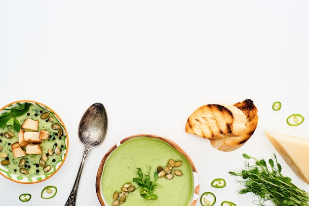 Фото Вид сверху на вкусный сливочно-зеленый овощной суп с ростками, жареными гренками и изолированным сыром
