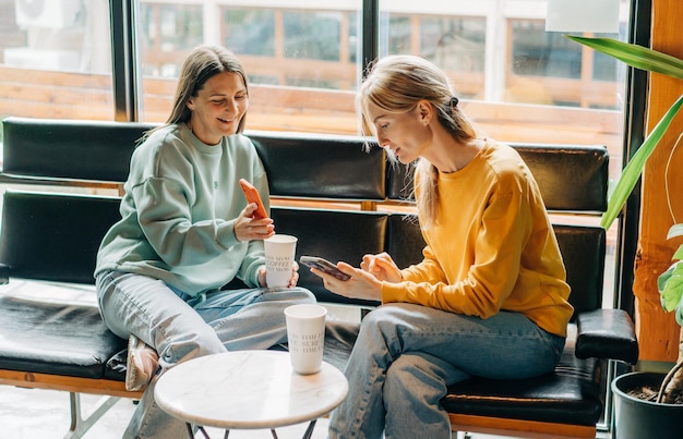 Фото Две веселые смеющиеся подруги в кафе общаются и общаются по телефону
