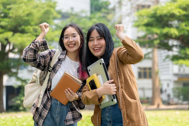 Фото Две возбужденные азиатские студентки поднимают кулаки в знак празднования, стоя на открытом воздухе.