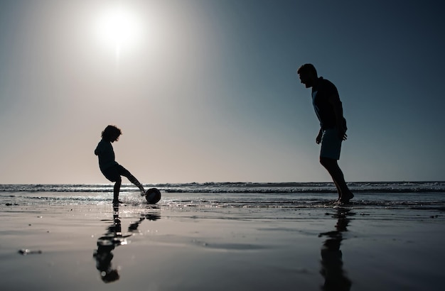 Vader en zoon voetballen of voetballen op het strand tijdens gezinsvakanties in de zomer
