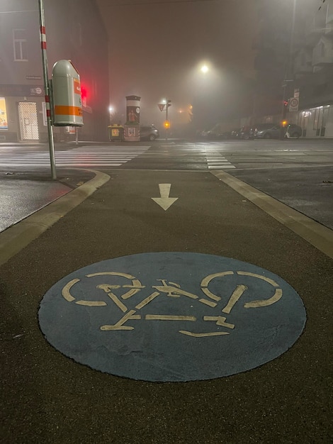 Вертикальный снимок знака велосипедной дорожки, нарисованного на бетонных пустых городских улицах в тумане на заднем плане