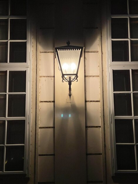 Вертикальный снимок старинного уличного фонаря, светящегося в темноте, висящего на стене дома