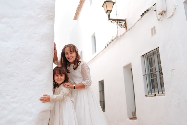 매우 아름다운 백인 자매, 친교 드레스를 입고 꽃과 함께 흰 드레스를 입은 소녀, 마을 Cadiz의 흰 벽이있는 일부 거리에서
