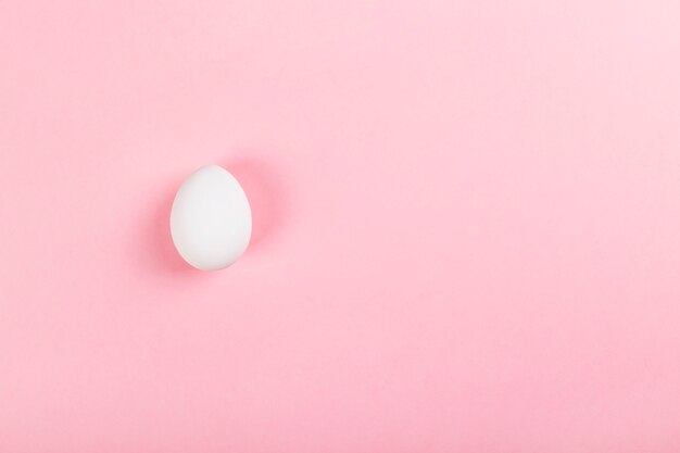 White egg on pink background. Top view, copy space