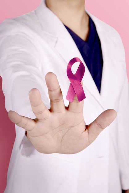 Женщина-врач в белом лабораторном халате с жестом стоп и показом розовой ленты на пальце