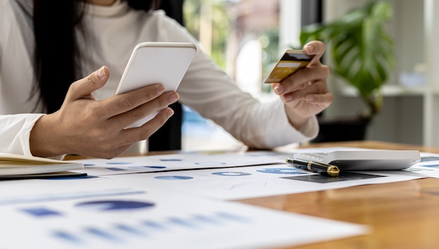 A woman holding a smartphone and a credit card, she is doing online shopping through a smartphone app by paying credit card payments. Online shopping ideas with a credit card.