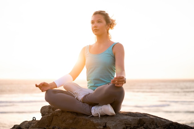 Женщина практикует йогу в позе лотоса для медитации с летними каникулами скалистый пляж счастье и расслабление Спокойные женские упражнения с йогой медитируют на океанском пляже с золотым временем заката
