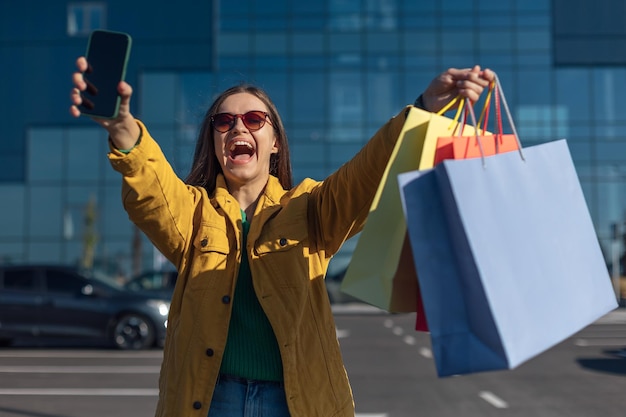 Женщина подняла руки вверх со смартфоном и сумкой с продуктами