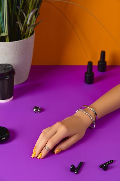 Womans hand with jewelry accessories nail varnish bottle and paper cup over purple table