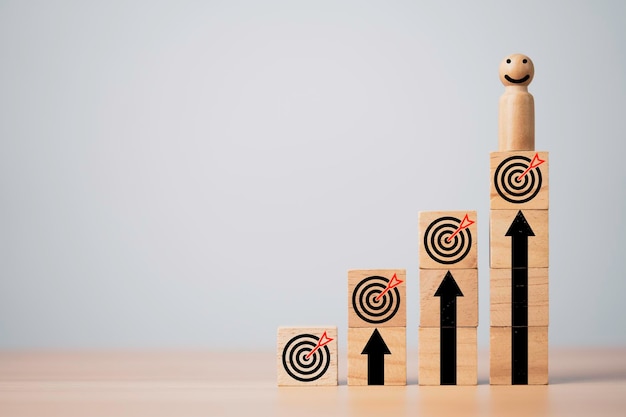 Фото Деревянная миниатюрная фигура с улыбкой и стоящей на вершине доски с стрелой для достижения бизнес-цели, цели и концепции цели