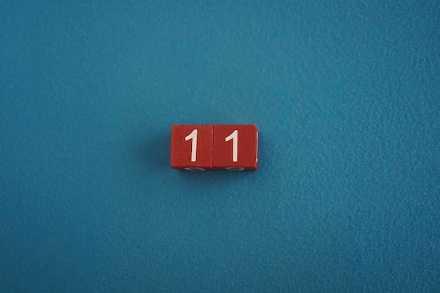 Фото Деревянные кубики viva magenta с номером 11 на синем фоне крупный вид сверху концепция даты или времени белые цифры 11 на красных кубиках бархатный фон копируйте пространство для текста или события образовательные кубики