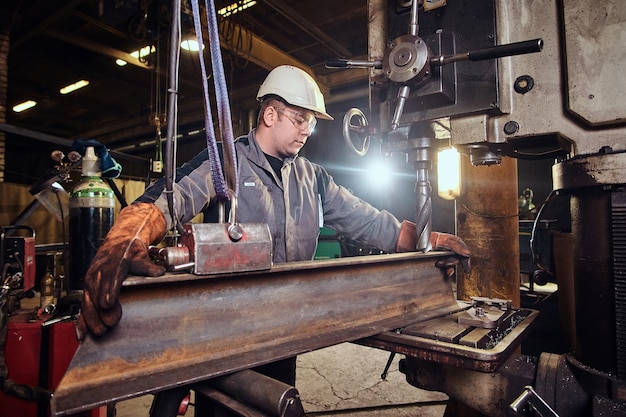 Рабочий в защитном шлеме проверяет тяжелый кусок рельса на металлургическом заводе.