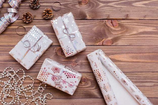 Photo wrapped in festive packaging gift boxes tied with silver ribbon, a roll of wrapping paper and christmas decorations on a wooden table. preparing for christmas.