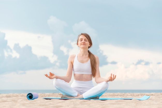 Йога на рассвете на пляже Молодая красивая женщина практикует медитацию йогой на открытом воздухе у моря