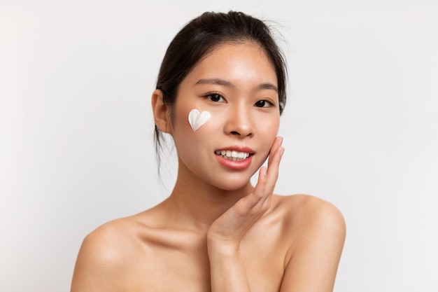 Photo youth skincare concept young korean lady with heartshaped moisturizer cream on face posing over