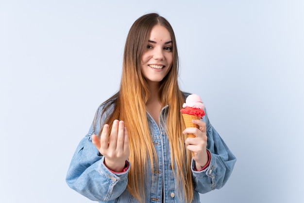 Young woman with a cornet ice cream on blue wall inviting to come with hand. Happy that you came
