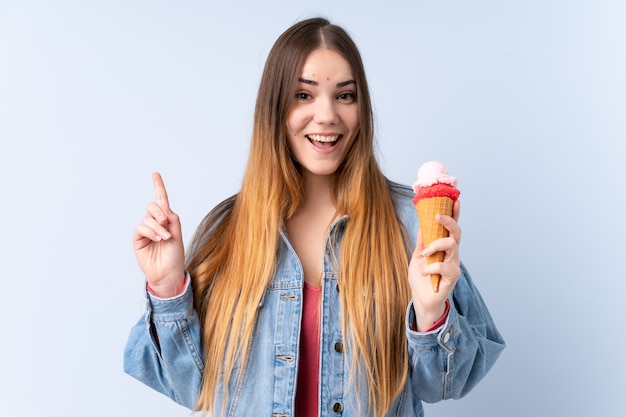 Young woman with a cornet ice cream isolated on blue wall pointing up a great idea