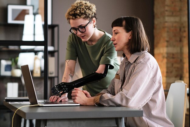 Фото Молодая женщина с протезом руки указывает на ноутбук и разговаривает со своим коллегой во время работы в офисе