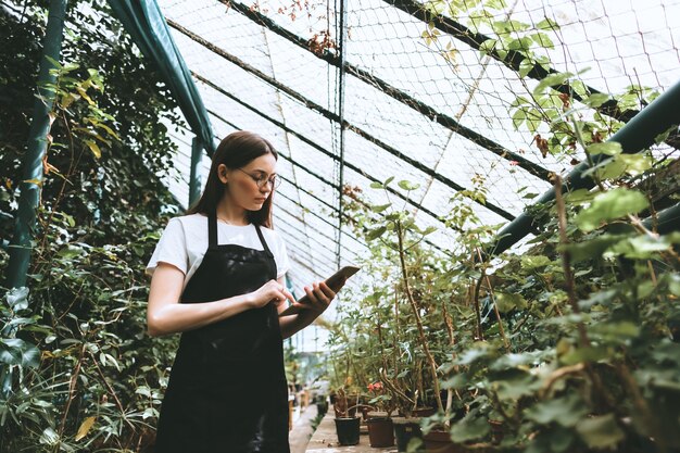 Young woman gardener with digital tablet working in a greenhouse.