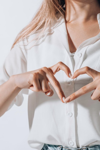 Фото Молодая женщина в рубашке делает жест сердца пальцами перед грудью, показывая любовь
