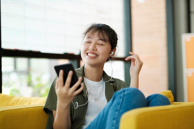 Молодая азиатка улыбается, слушая музыку с помощью смартфона дома