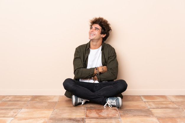 Photo young caucasian man sitting on the floor looking up while smiling