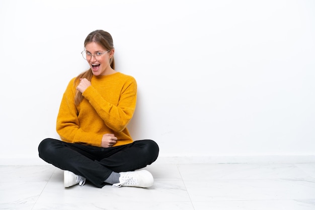 Photo young caucasian woman sitting on the floor isolated on white background celebrating a victory