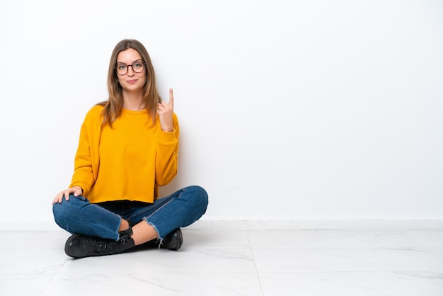Photo young caucasian woman sitting on the floor isolated on white background pointing with the index finger a great idea