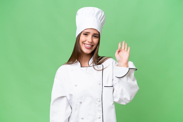 Young chef caucasian woman over isolated background saluting with hand with happy expression
