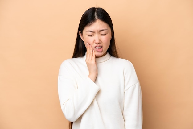 Young Chinese woman isolated on beige background with toothache
