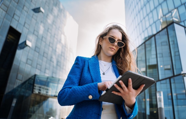 Фото Молодая уверенная в себе женщина в костюме с помощью планшета темная атмосфера бизнесменка идет в офис