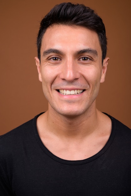 Young handsome Hispanic man on brown wall