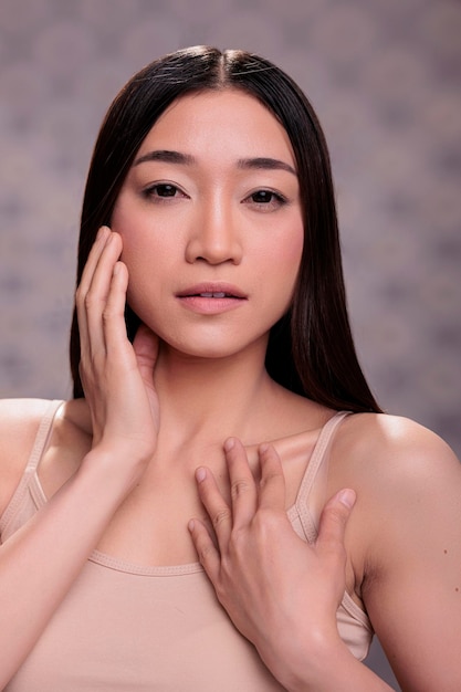Photo young natural beautiful asian model posing for cosmetology fashionable portrait, touching smooth healthy skin after face spa treatment. woman putting arms on face and body in trendy pose
