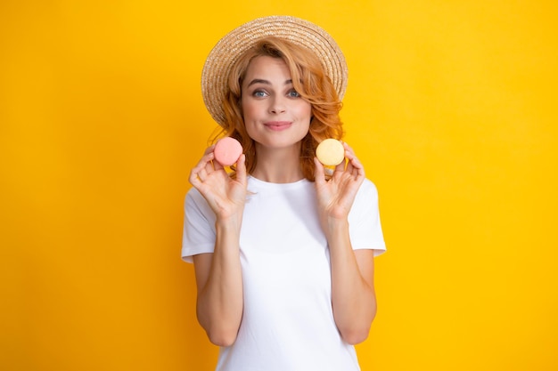 Фото Молодая довольная женщина, изолированная на желтом фоне, ест миндальное печенье девушка ест французские макаруны