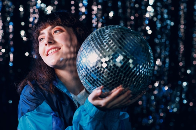 Фото Молодая спортивная женщина 80-х и 90-х годов в стиле 90-х модная позитивная девушка на дискотеке в ночном клубе с диско-шаром