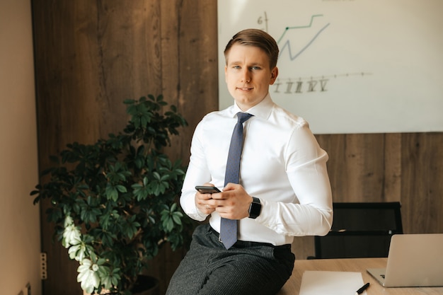 Photo young successful male businessman holding a smartphone in his hands. communication technologies.