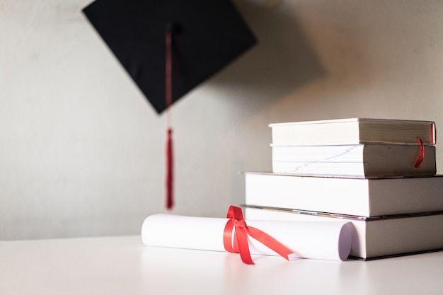 Фото Выпускная шляпа или ступка и дипломный сертификат, перевязанный красной лентой на стопке книг с пустым пространством, слегка ненасыщенным виньеткой для создания винтажного эффекта