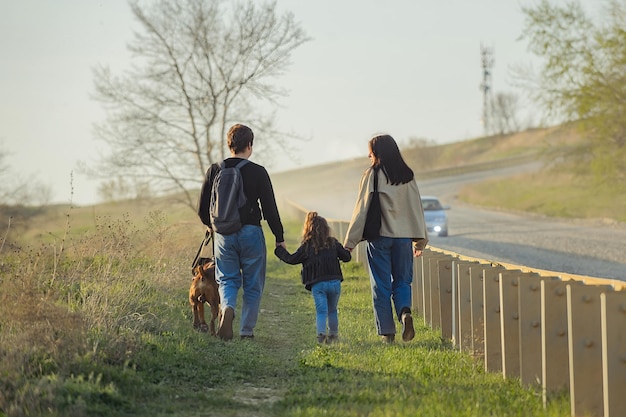 사진 3명의 젊은 가족과 개가 길을 따라 걷는다