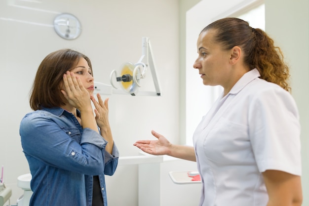 Взрослая женщина страдает от зубной боли и жалуется во время визита к профессиональному стоматологу