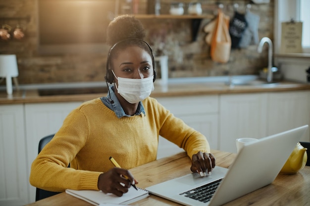African American female entrepreneur with protective face mask working on laptop at home