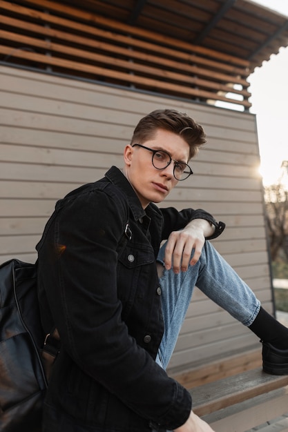 Фото Американский молодой человек в модной повседневной джинсовой одежде в стильных очках с модным черным рюкзаком