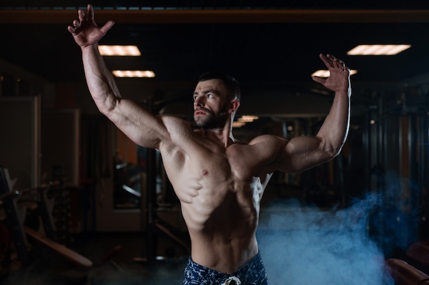 Спортивный человек с мускулистым телом позирует в тренажерном зале, демонстрируя свои мышцы