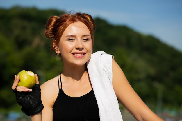 Фото Привлекательная рыжая кавказская девушка ест яблоко после спортивной тренировки. место для текста